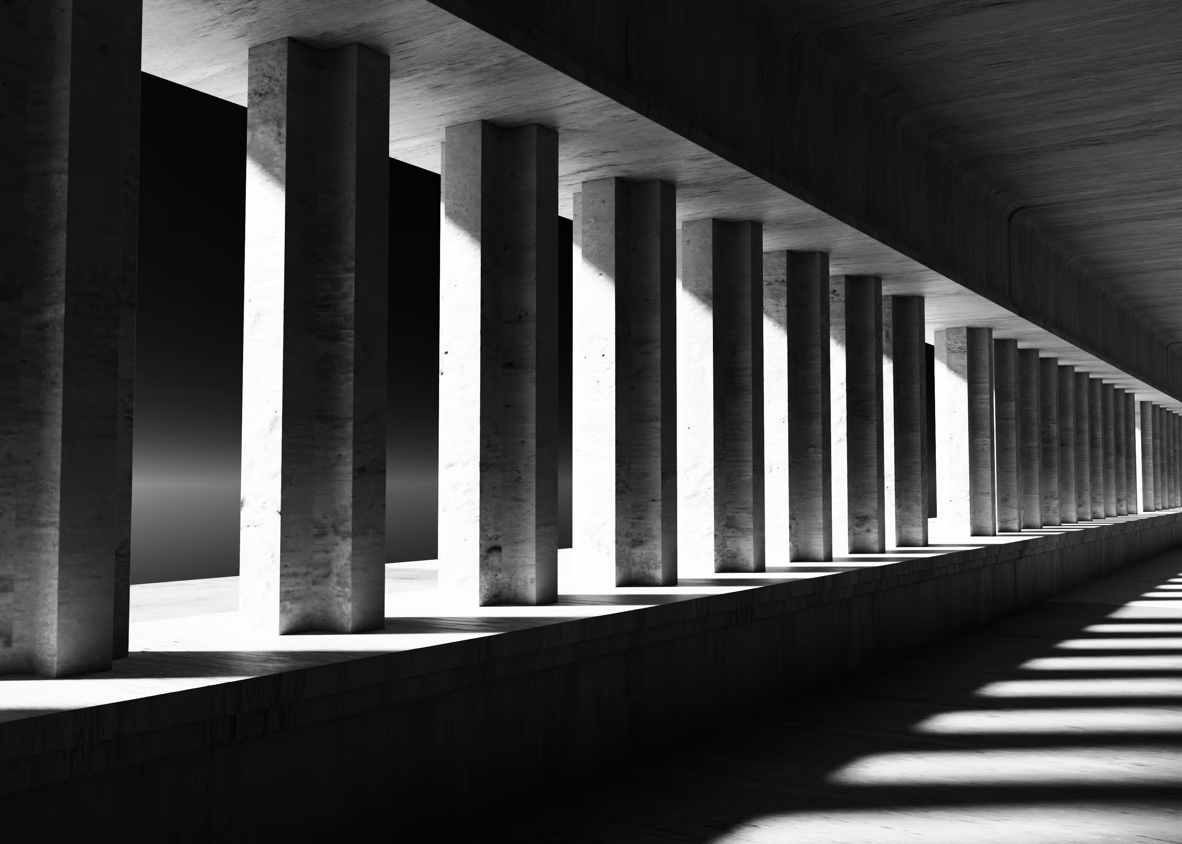 Black and white view of a corridor with evenly spaced vertical concrete pillars casting long shadows.